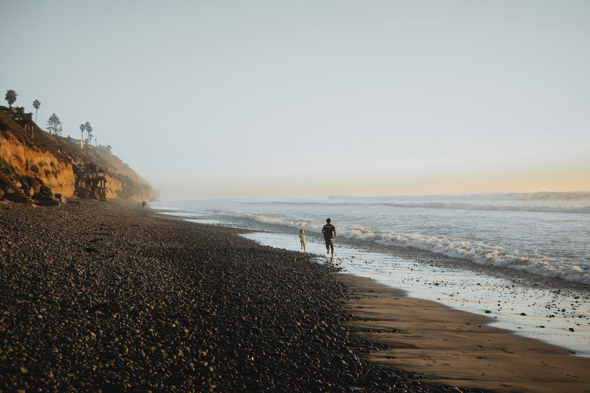 A parent and child running along the cobblestone shoreline at golden hour in Encinitas