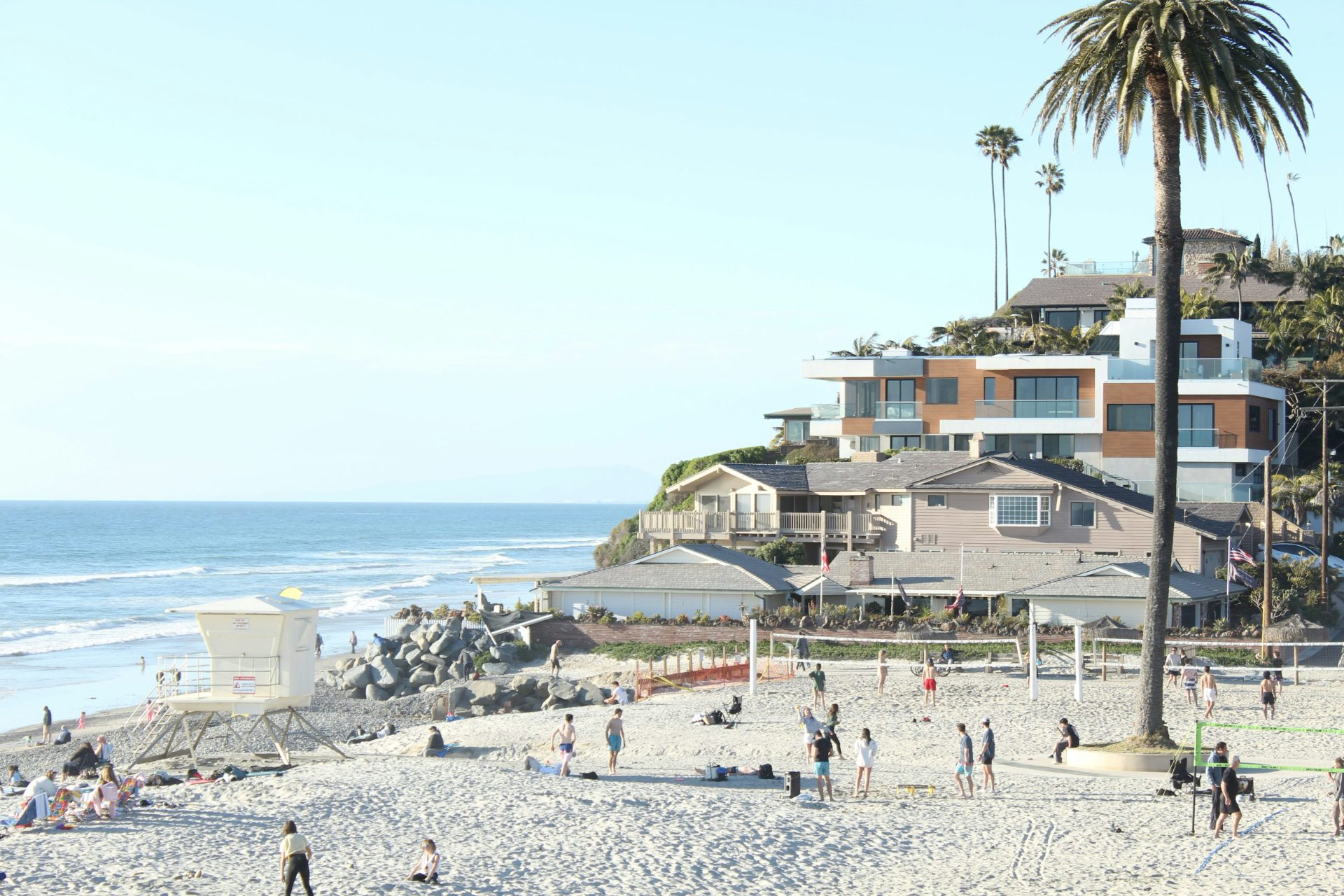 Volleyball nets and beachgoers on the sand at Moonlight Beach, homes on the hill behind